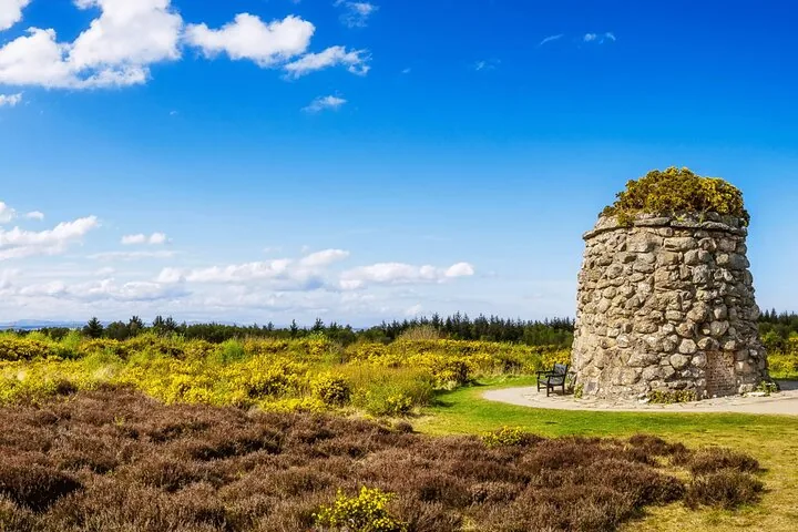 Stone memorial cairn with a bench at Culloden Battlefield under a blue sky