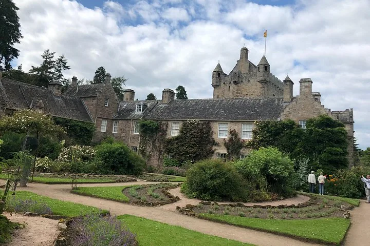 Cawdor Castle surrounded by manicured gardens and visitors on a cloudy day