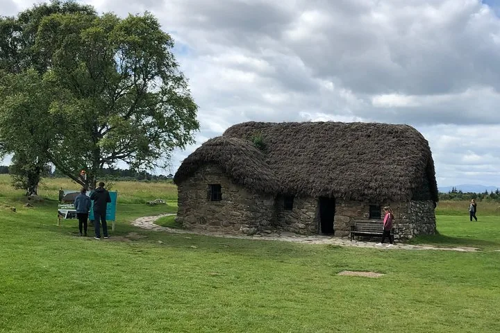 Traditional thatched-roof stone cottage at Culloden Battlefield with visitors nearby